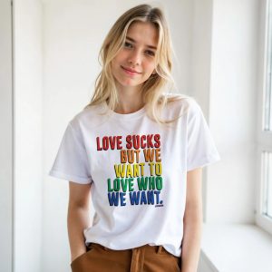 Ragazza bionda che indossa una t-shirt bianca con scritta arcobaleno “LOVE SUCKS BUT WE WANT TO LOVE WHO WE WANT”.